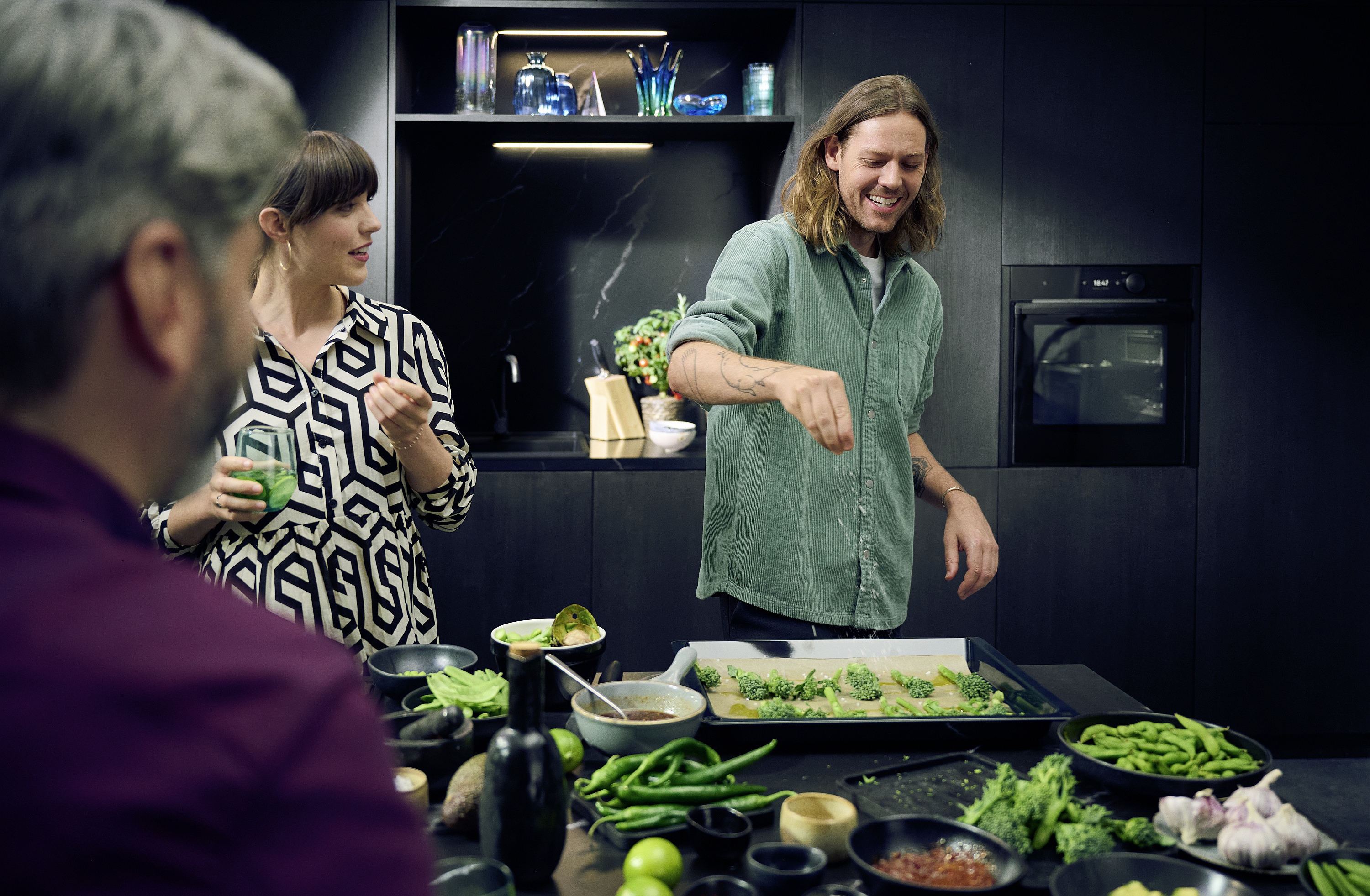 Eine Gruppe junger Menschen beim Zubereiten von grünem Gemüse in dunkler moderner Küche